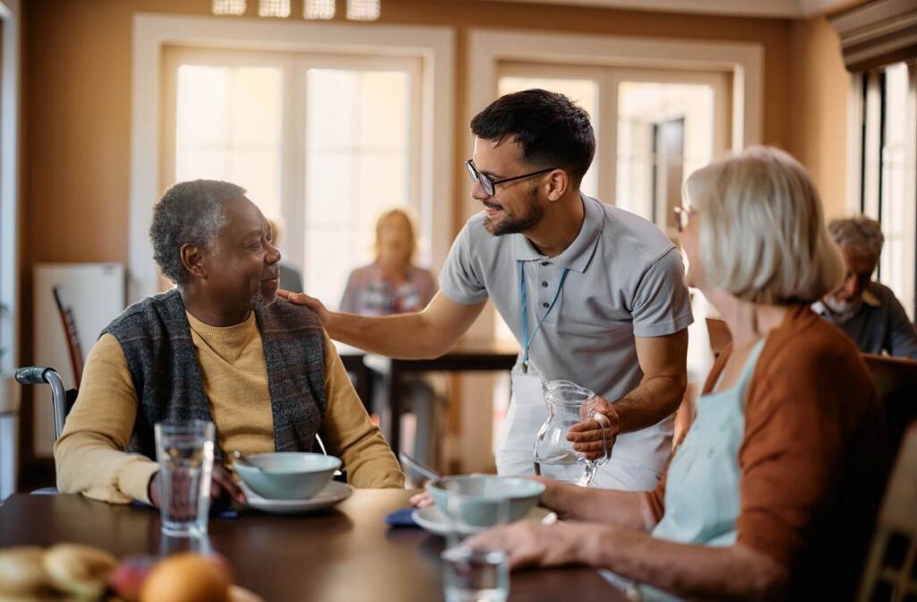 an assisted living carer speaks to seniors at a dining table