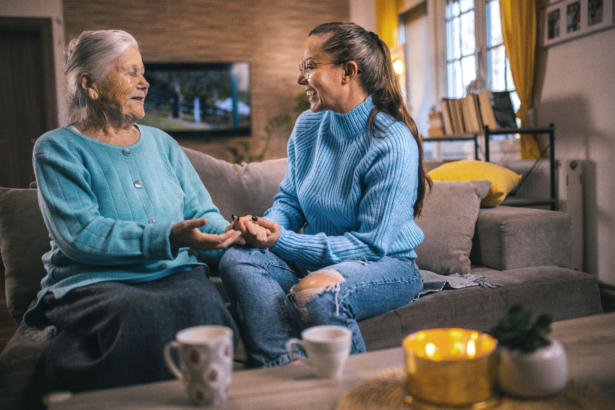 An elderly woman and an older adult speaking to each other while drinking a cup of tea.